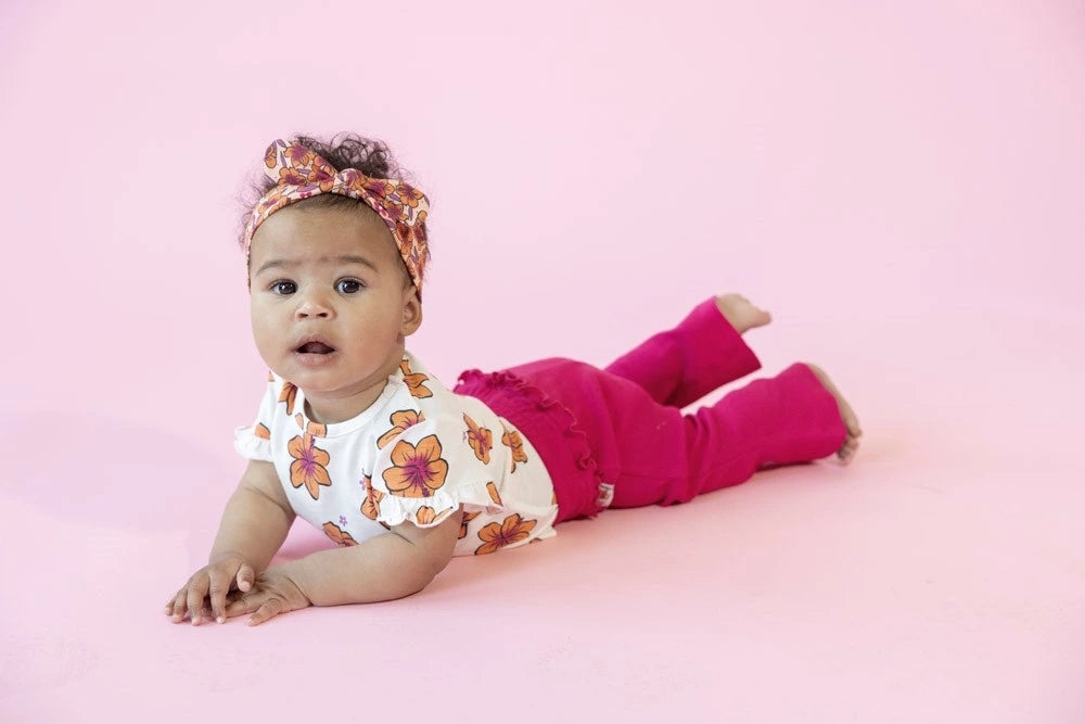 Baby in een kleurrijk babyshirt, met fuchsiabroek op oorspronkelijke roze achtergrond.