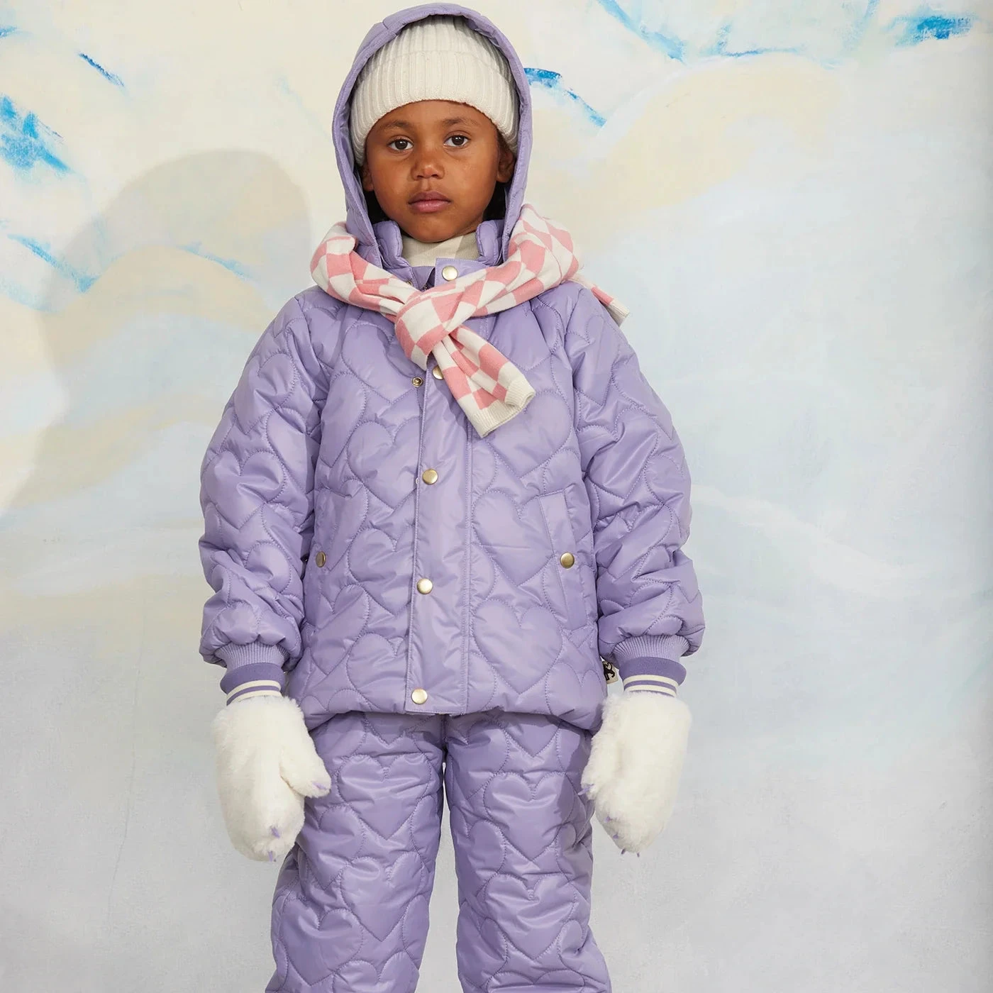 Kind met Mini Rodini-muts, sjaal en wanten bij een lila jas
