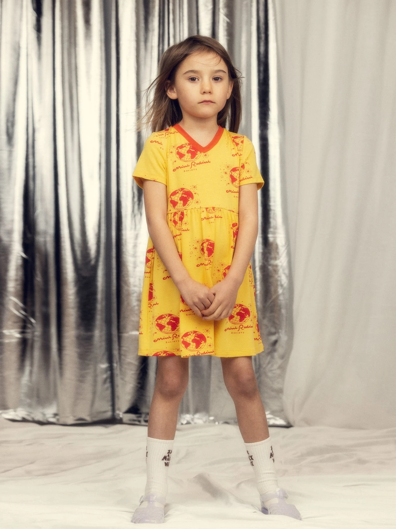 Kind in een gele Mini Rodini-jurk met rode wereldbollen