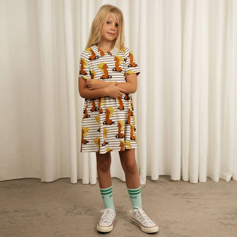 Kind in een gestreepte Mini Rodini-jurk met zeepaardjes