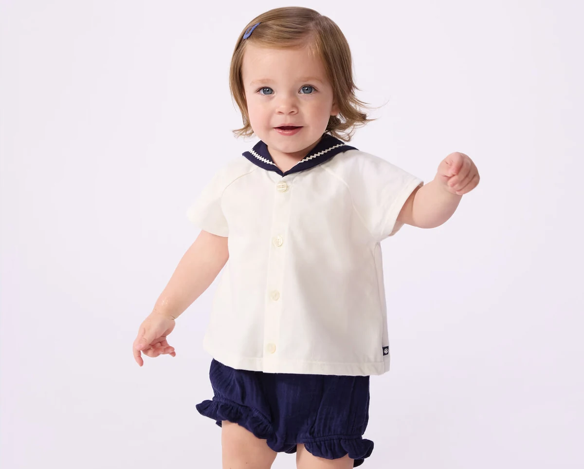 Baby in een witte top met matrozenkraag en donkerblauw Petit Bateau-broekje
