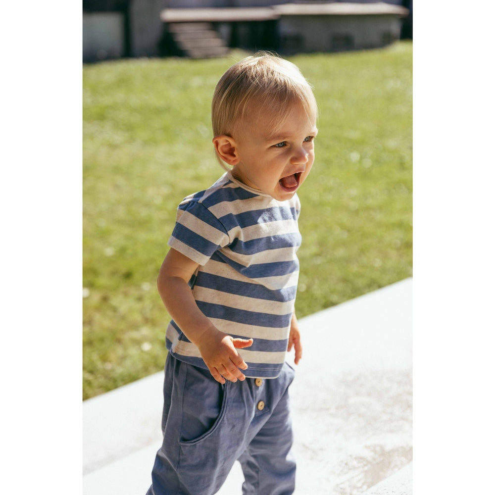 Kind in het blauwe Snug T-shirt met witte print, buiten in het gras